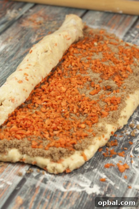 Chef rolling out carrot cake cinnamon roll dough on a lightly floured surface.