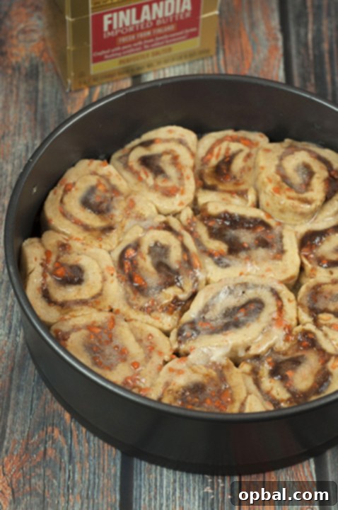 Unbaked carrot cake cinnamon rolls with mascarpone icing arranged in a baking dish, ready for the oven.