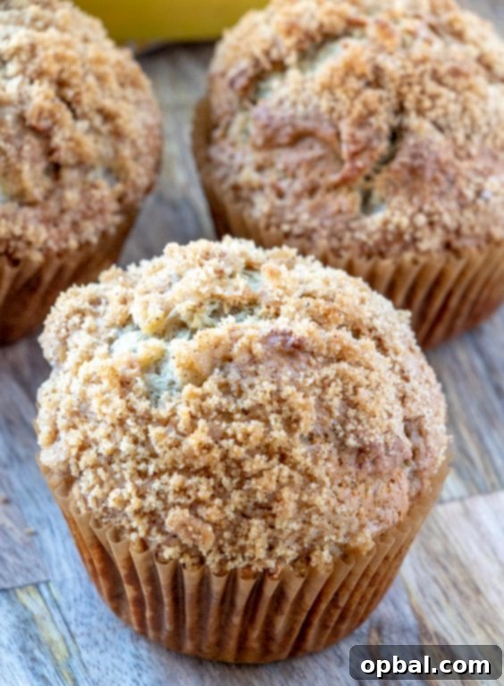 A close-up of a perfectly baked banana crumb muffin, featuring a thick, buttery streusel topping.