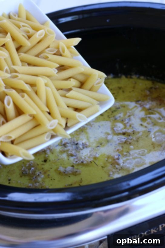 Slow Cooker Creamy Chicken Alfredo 5 Adding penne pasta to the alfredo sauce in a crock pot.