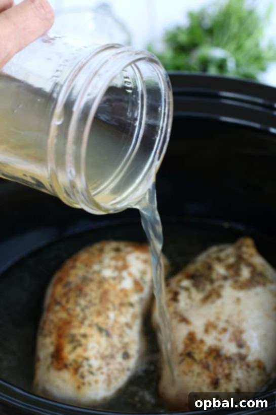 Slow Cooker Creamy Chicken Alfredo 7 Pouring chicken stock into a crockpot to add flavor to the chicken in alfrdo sauce.