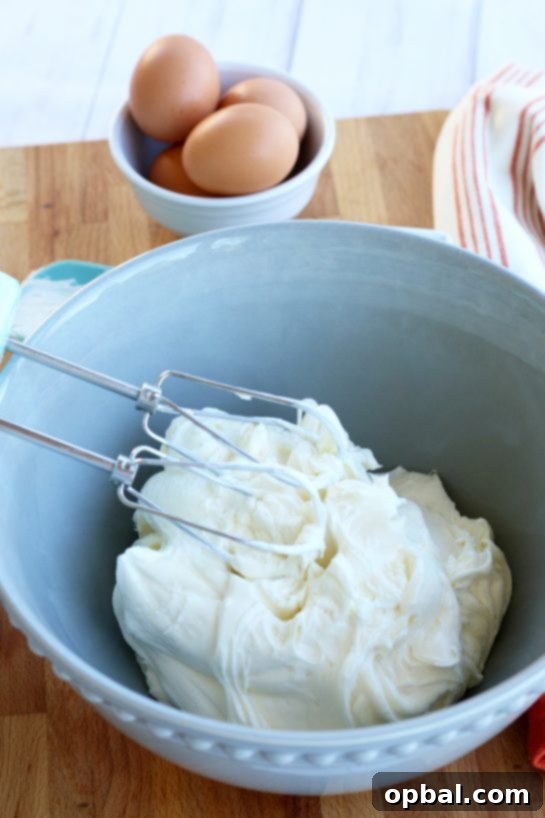 Pumpkin Spice Cheesecake Bars 9 Softened cream cheese being whipped to perfection with a hand mixer in a beautiful blue mixing bowl.