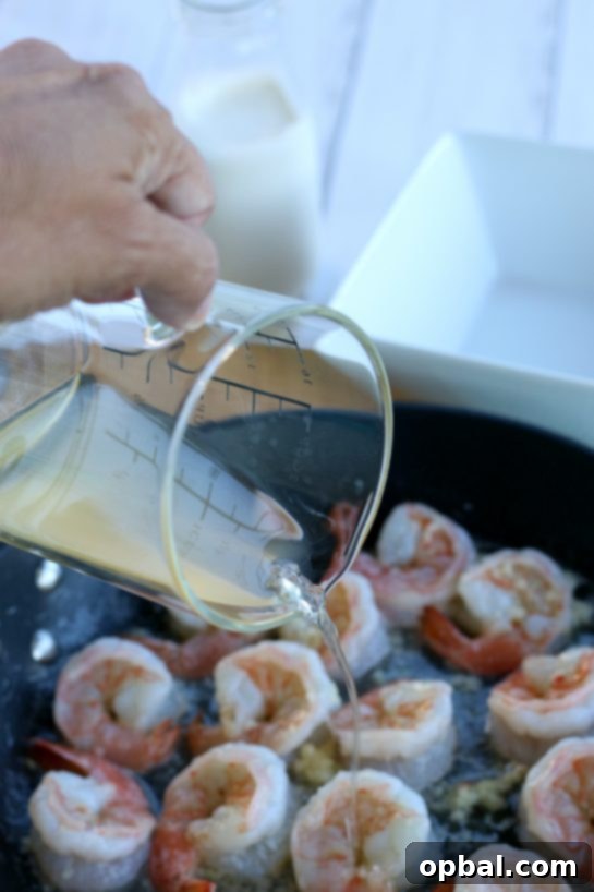 Garlic Butter Shrimp in a Velvety Cream Sauce 5 Adding rich chicken broth to the sizzling shrimp and garlic in a skillet, a crucial step in building the creamy garlic butter sauce.