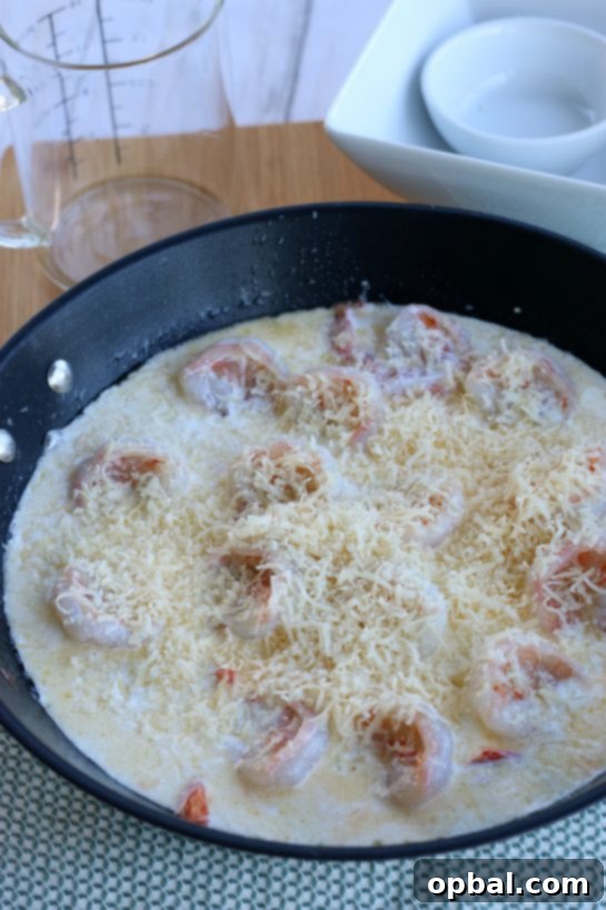 Freshly grated Parmesan cheese being generously sprinkled over the simmering garlic butter shrimp and creamy sauce, adding the final touch of flavor and richness.