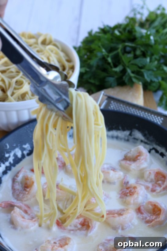 Perfectly cooked pasta being added to the rich and creamy garlic butter shrimp sauce in a skillet, ready to be tossed together for a complete meal.