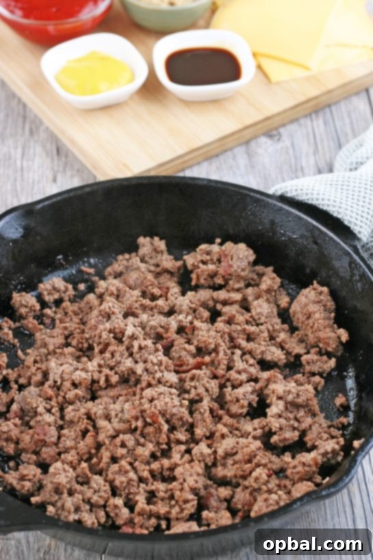 Cheeseburger Biscuit Poppers 5 A close-up shot of ground beef sizzling and browning in a hot skillet, the first crucial step in preparing the flavorful filling for the cheeseburger biscuit bites.