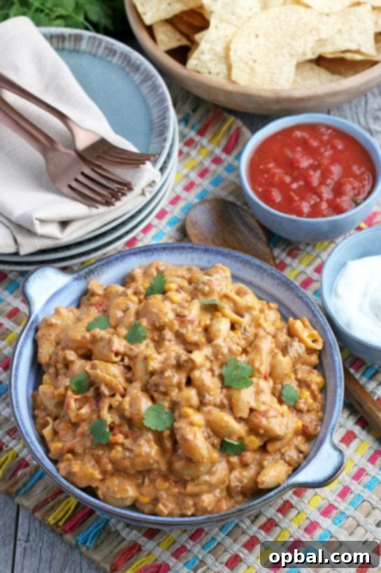 Easy Crockpot Creamy Taco Pasta 12 A view of the table with a bowl full of Mexican pasta salad, accompanied by tortilla chips, salsa, and silverware, set for a delightful meal!