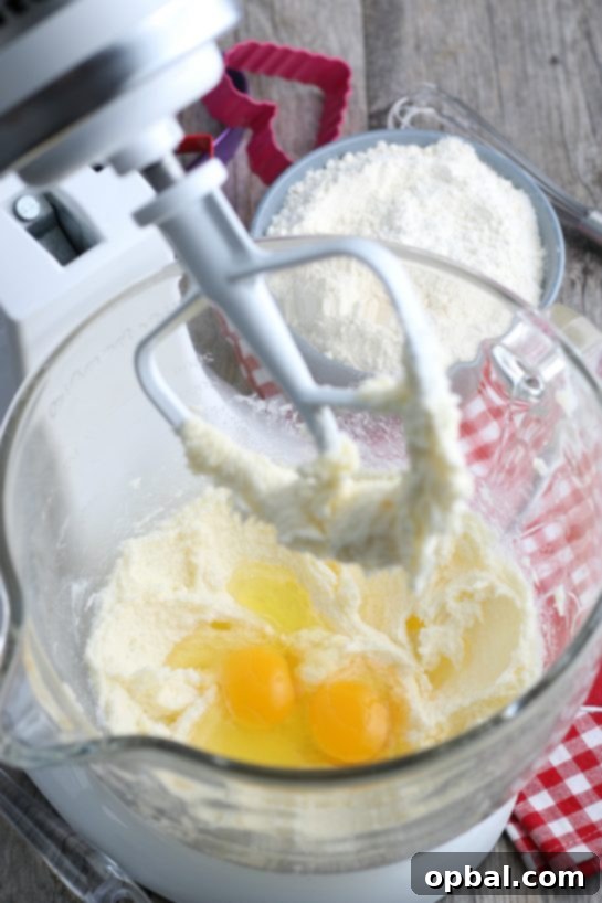 Crafting Edible Love Notes: Decorating Valentine's Conversation Heart Cookies 8 A close-up view within a stand mixer as large eggs are gently added to the creamy, aerated batter, marking the next step in preparing the dough for our delightful decorated sugar cookies.