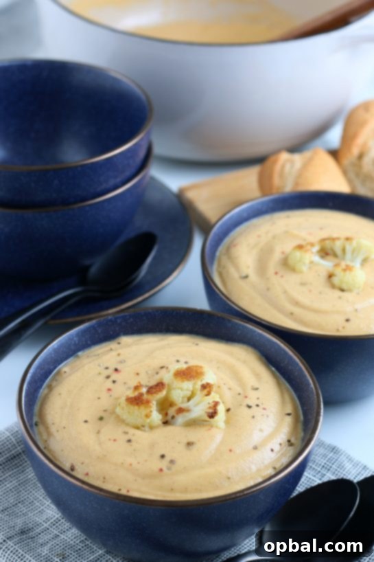 A final close-up of the roasted cauliflower soup, beautifully presented in a rustic bowl with extra roasted florets and fresh herbs for garnish, inviting a delicious tasting.