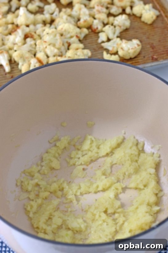 Diced yellow onions, minced garlic, cumin, and coriander cooking in a Dutch oven with olive oil, creating a fragrant base for the roasted cauliflower soup.
