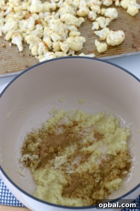 A generous sprinkling of salt, pepper, cumin, and coriander over roasted cauliflower florets, highlighting the essential seasonings that give this soup its flavorful depth.