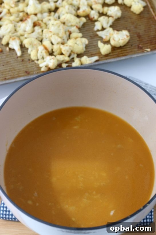 A pot of simmering vegetable broth infused with sautéed onions, garlic, cumin, and coriander, creating a rich base for the cauliflower soup.