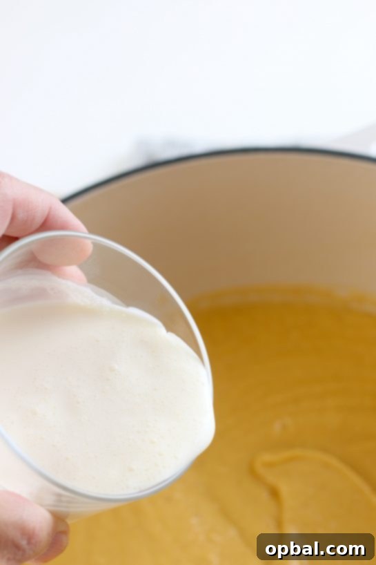 Heavy cream being poured into the blended roasted cauliflower soup, adding richness and achieving its desired smooth, creamy consistency before serving.