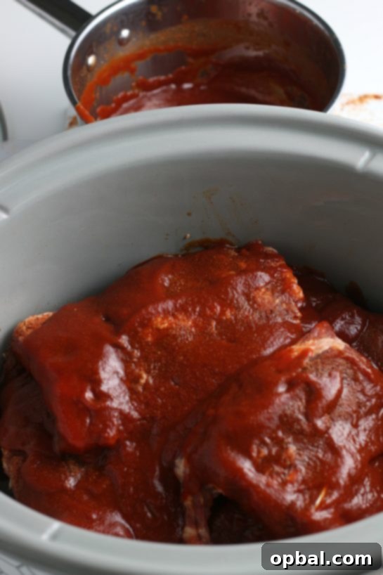 Close-up of ribs nestled in the slow cooker, ensuring each piece is fully coated in the delicious sauce for maximum juiciness.