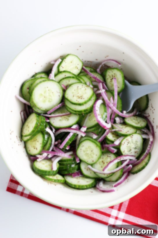 The cucumber salad being made by mixing the cucumber and onions with dressing, showing the blending process.