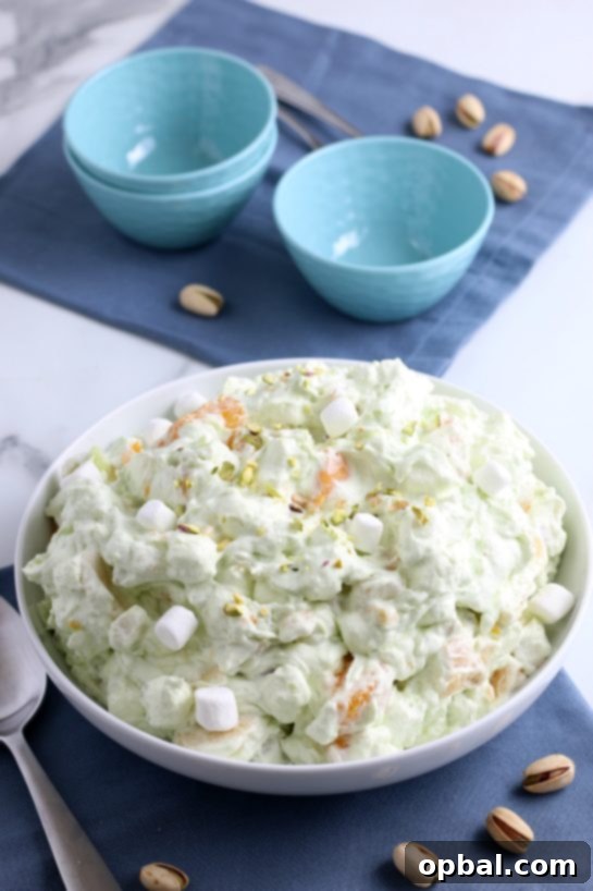 Pistachio Cloud Fruit Ambrosia 2 A vibrant green pistachio fluff salad presented beautifully in a large serving bowl, surrounded by smaller individual dishes ready for guests. This classic dessert is perfect for any gathering.