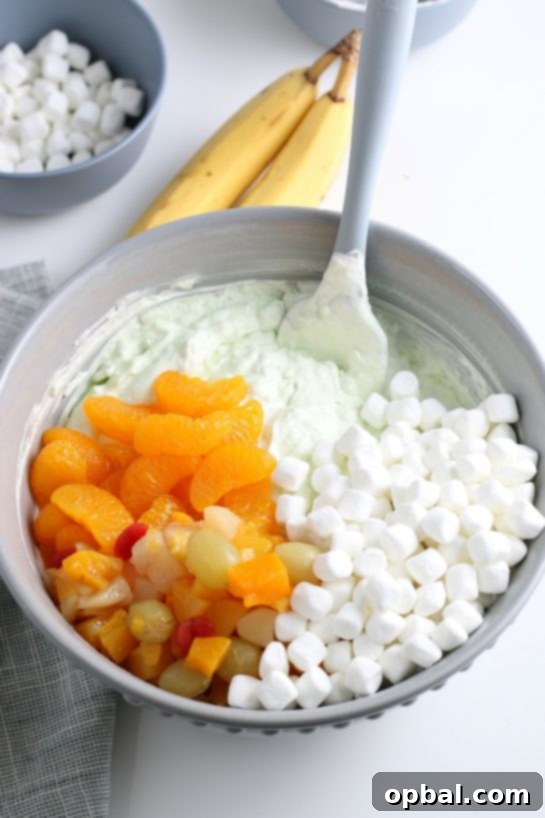 Pistachio Cloud Fruit Ambrosia 13 Adding a generous amount of mixed fruit to the Watergate Salad recipe, ensuring every bite is bursting with diverse textures and sweet flavors.