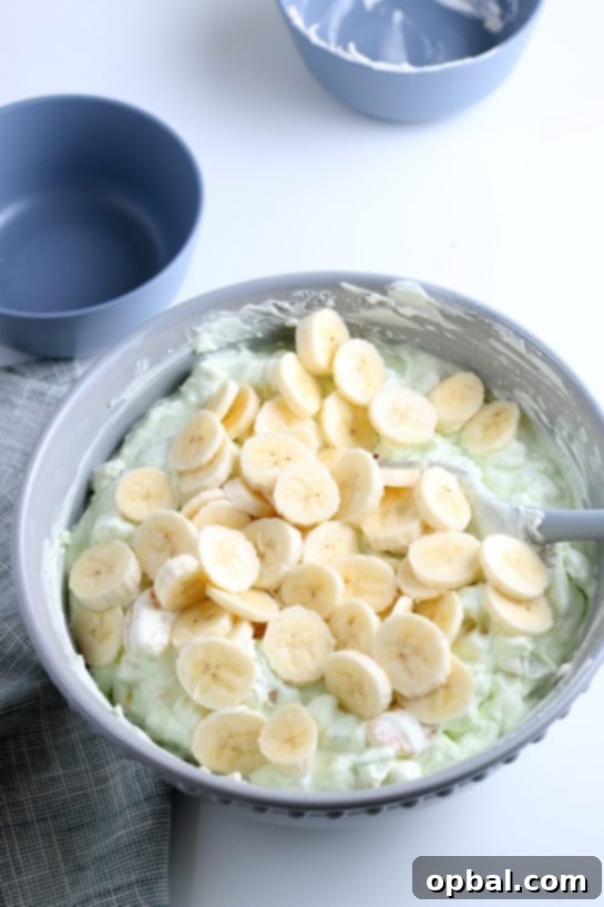 Pistachio Cloud Fruit Ambrosia 14 Sliced fresh bananas being carefully added to the creamy pistachio salad mixture, contributing a soft texture and natural sweetness.