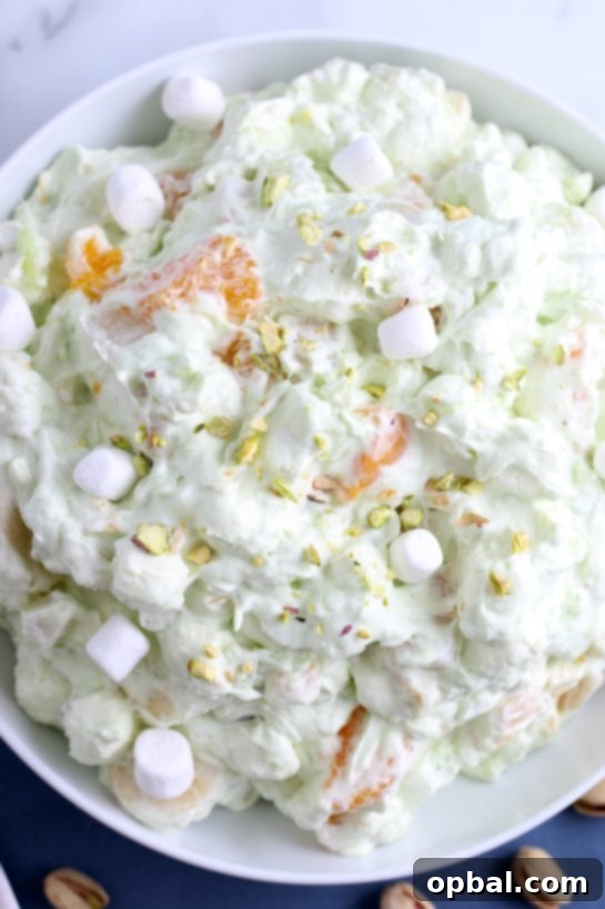 Pistachio Cloud Fruit Ambrosia 7 The final step of preparing pistachio salad, showing a sprinkle of chopped pistachios being added on top for garnish and extra crunch.