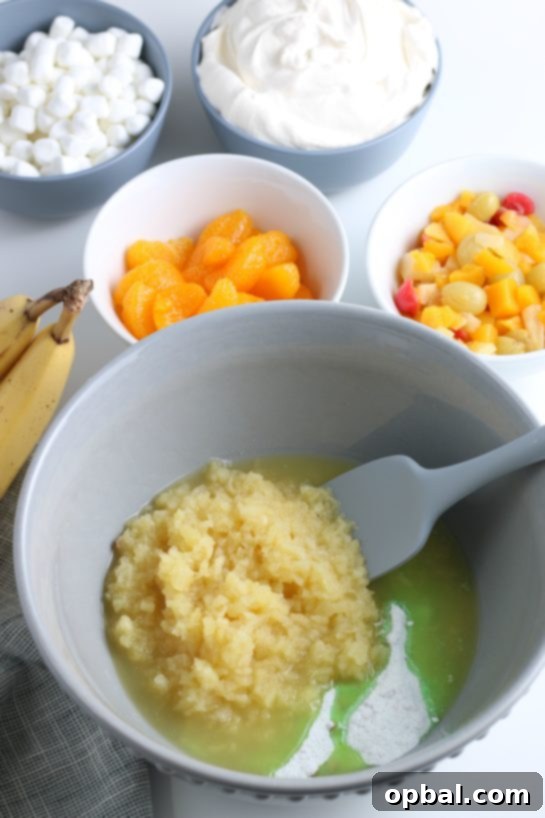 Pistachio Cloud Fruit Ambrosia 10 The initial step of combining the dry pistachio pudding mix with the crushed pineapple in a large mixing bowl.