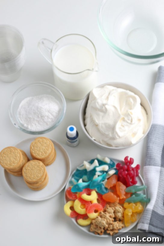 Seaside Pudding Parfaits 4 Essential ingredients for crafting delectable Beach Sand Pudding Cups, including instant vanilla pudding mix, cold milk, whipped topping, blue food coloring, Golden Oreos, and various gummy candies.