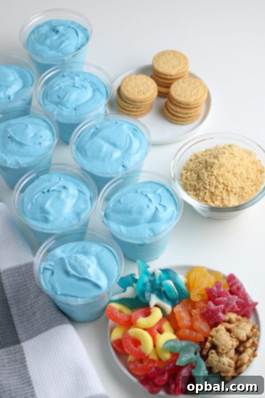 Seaside Pudding Parfaits 9 Pouring the vibrant blue pudding mixture into clear plastic cups, creating the base for the delightful Beach Sand Pudding Cups.