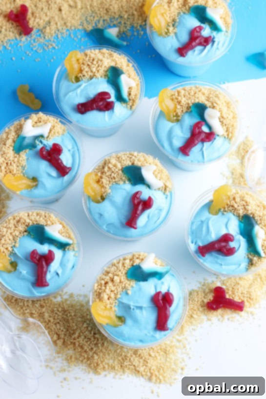 Seaside Pudding Parfaits 10 Beautiful blue Beach Sand Pudding Cups, a delightful and easy no-bake dessert for kids, made with vanilla pudding, food coloring, whipped topping, and garnished with playful gummy sea creatures.