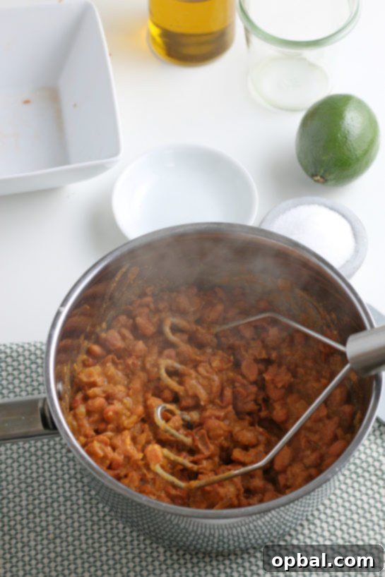 Mashing the cooked pinto beans with a potato masher to achieve the perfect refried bean texture