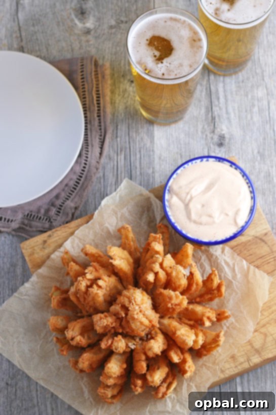 Golden Blossom Onion 14 An overhead shot of a perfectly fried blooming onion, fanned out and presented with a generous serving of homemade dipping sauce. The ultimate appetizer recipe, transforming a sweet onion into an incredibly delicious and visually stunning snack!