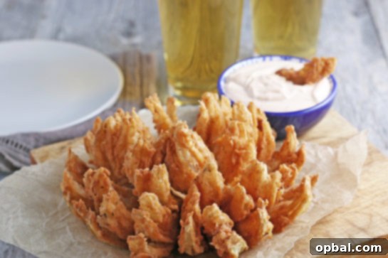 Golden Blossom Onion 3 A close-up view of a perfectly fried blooming onion, showcasing its crispy texture and golden color. Served with a homemade dipping sauce, making it an incredibly delicious and must-try appetizer!