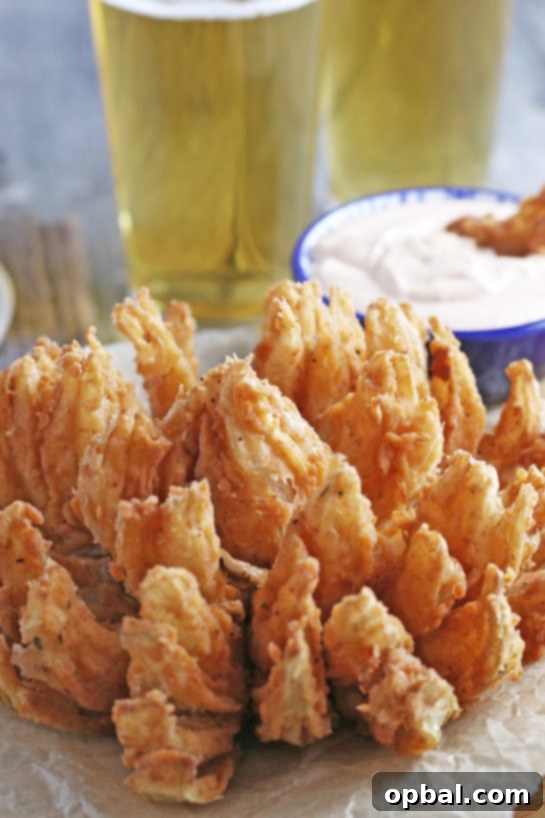 Golden Blossom Onion 7 A stunning close-up shot of a Fried Blooming Onion, showcasing its beautifully fanned-out petals and golden-crispy exterior. Served alongside a homemade dipping sauce, this appetizer is incredibly delicious and visually appealing.