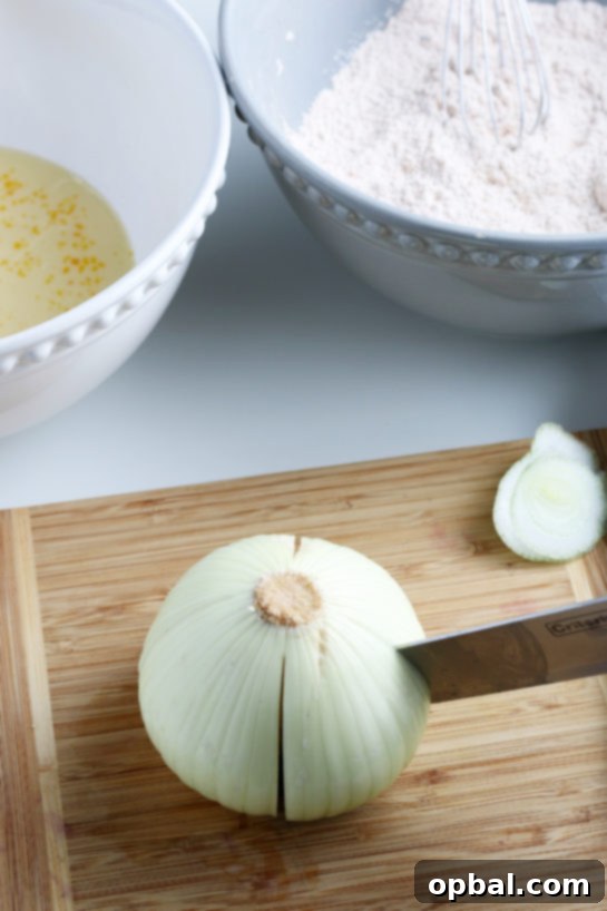 Golden Blossom Onion 10 A chef's knife carefully slicing a sweet onion, demonstrating the initial cuts for the blooming onion recipe.