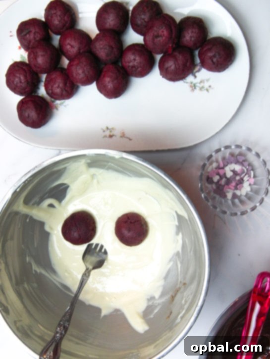 Dipping Red Velvet Truffles into melted white chocolate for coating.