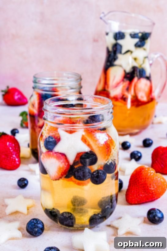 Freedom Sangria 2 A large glass pitcher filled with vibrant red, white, and blue patriotic sangria, garnished with fresh strawberries, blueberries, and star-shaped honeydew melon slices, ready to be served on a summer day.