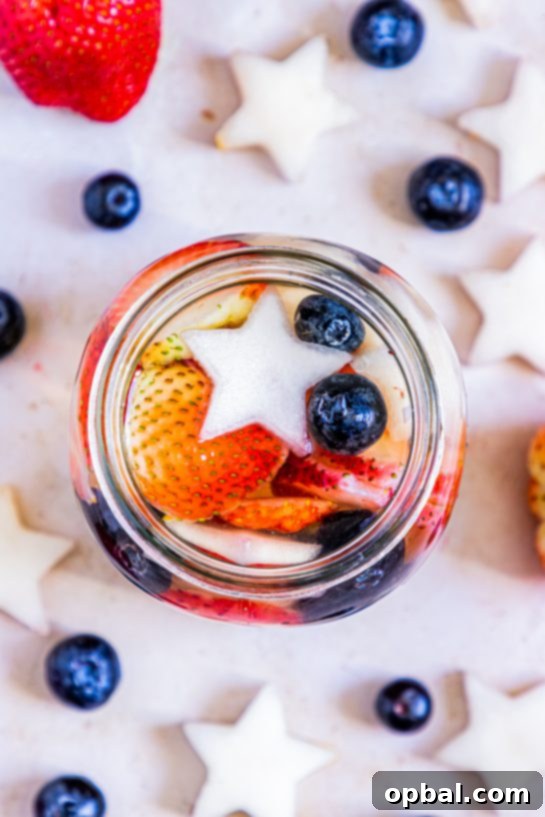 Freedom Sangria 6 Overhead view of a glass pitcher filled with patriotic sangria, featuring colorful fruit and ice, set on a bright surface for a festive summer gathering.