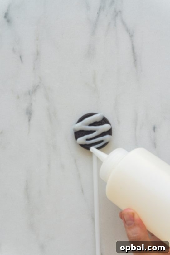 Halloween Mummy Oreo Pops 11 White icing being piped onto an Oreo with a lollipop stick to create the mummy wrap effect