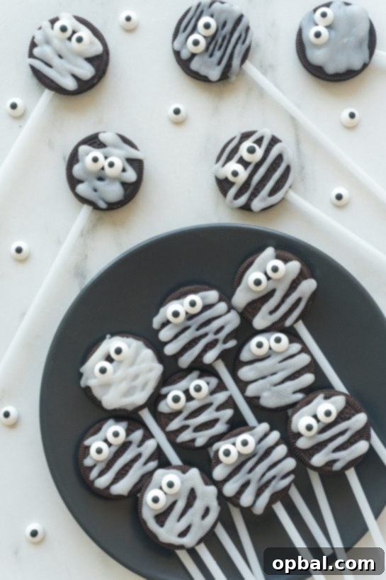 Halloween Mummy Oreo Pops 12 Overhead shot of several decorated Mummy Oreo Pops with varying expressions on their candy eyes, on a dark background