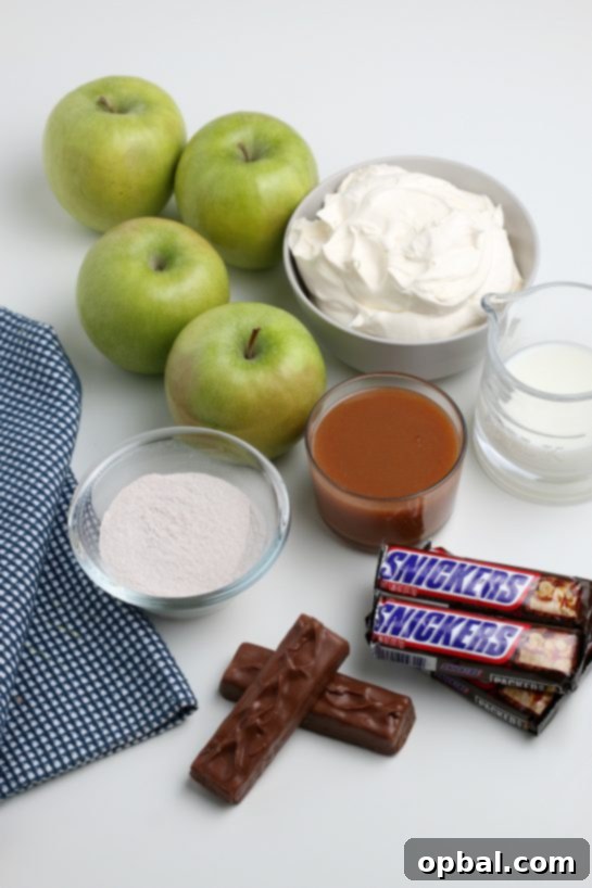 Caramel Apple Snickers Delight 3 A selection of fresh ingredients laid out, including crisp green apples, a package of whipped topping, and several Snickers candy bars, ready for preparing the Caramel Apple Snickers Salad.