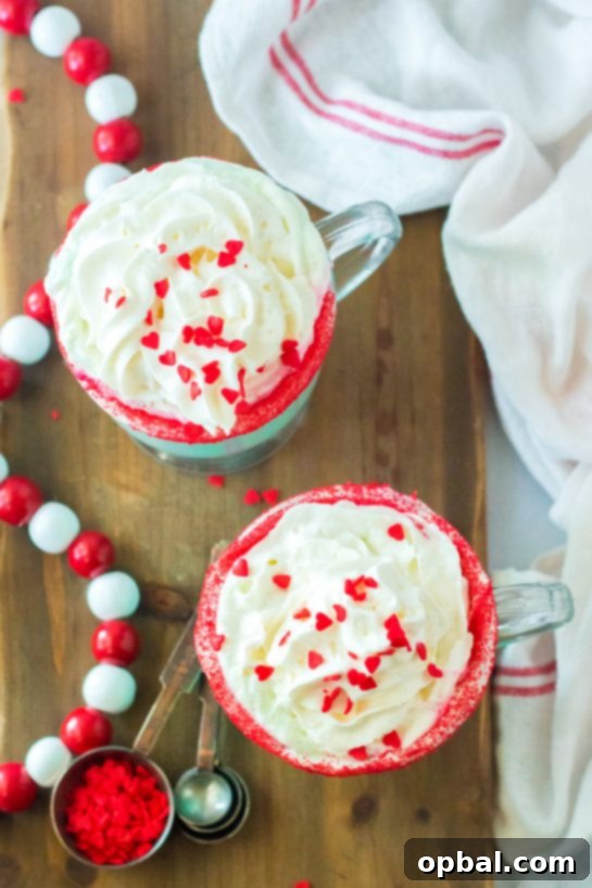 Grinchy Christmas Delight 3 Overhead shot of two mugs of Grinch Hot Chocolate, garnished with whipped cream and red candy hearts.