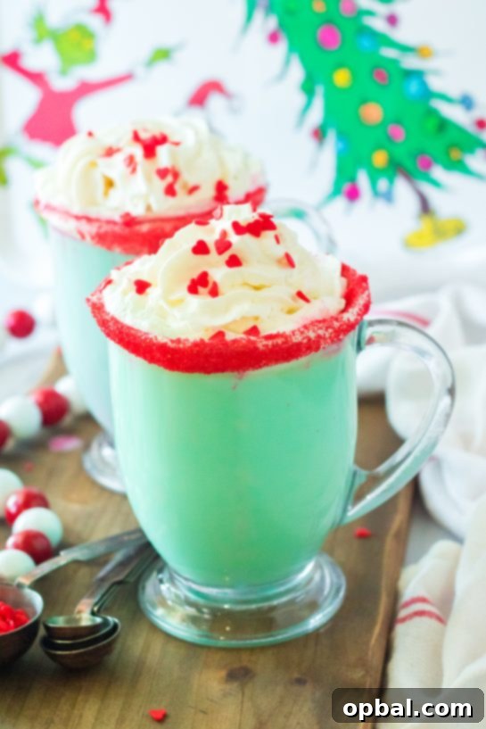 Grinchy Christmas Delight 8 A close-up of a festive mug of Grinch Hot Chocolate, adorned with whipped cream, red sprinkles, and a heart-shaped candy.