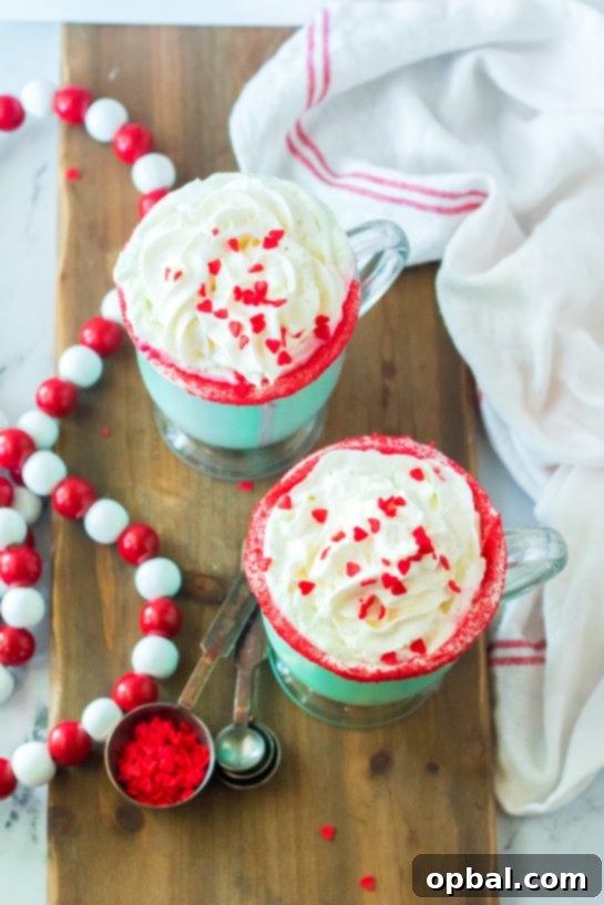 Grinchy Christmas Delight 11 Mug of Grinch Hot Chocolate with a festive sprinkle rim, whipped cream, and red sprinkles.