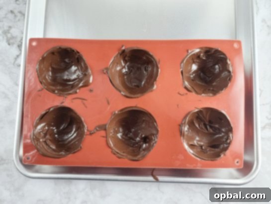Pouring melted chocolate into silicone molds to form half-spheres for the bombs.
