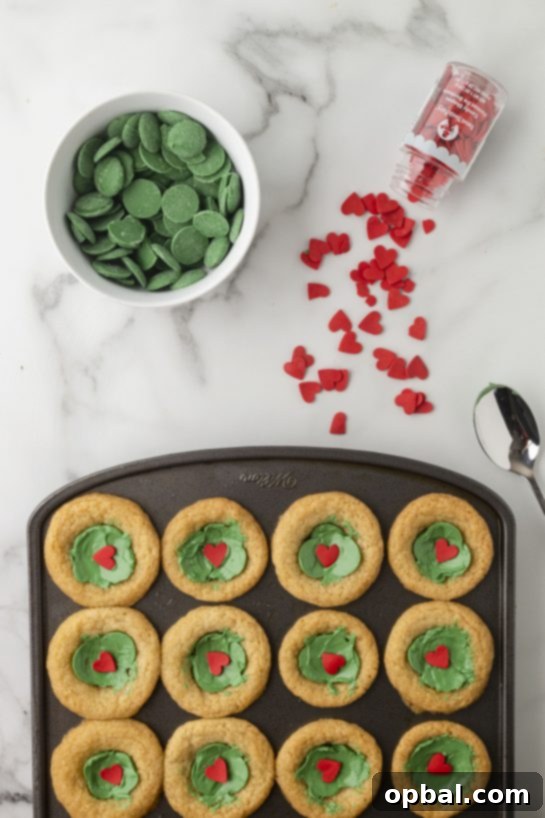 Grinchy Holiday Cookie Cups 5 Adding the green melting chocolates and red hearts for the Grinch Cookie Cup Bites recipe