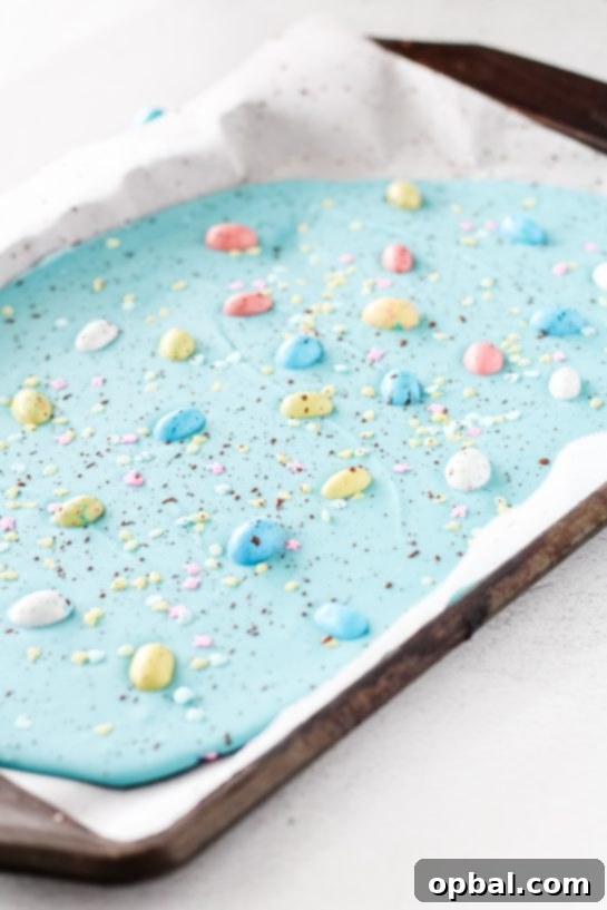 Speckled Robin's Egg Easter Bark 5 Decorating the blue chocolate bark with a mix of colorful sprinkles, a cocoa powder speckle, and festive Robin Eggs.