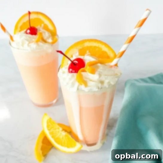 A tall glass of Orange Creamsicle Milkshake, topped with whipped cream and an orange slice, with a straw for sipping.