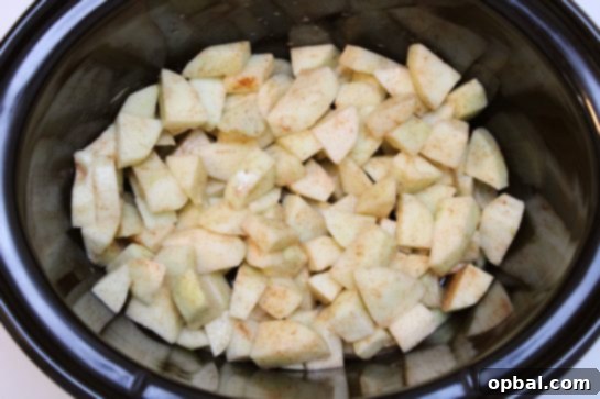 Sliced apples being poured into a slow cooker, ready for the crisp base