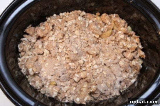 Buttery oat streusel topping being sprinkled over the apple mixture in the slow cooker