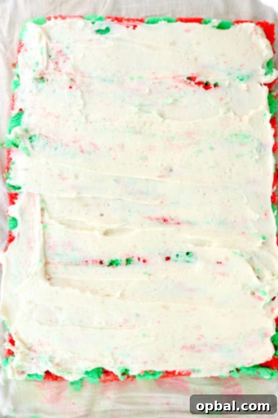 Festive Yule Log Cake 7 Carefully spreading the whipped frosting evenly across the baked cake in the jelly roll pan, ensuring full coverage before the final roll.