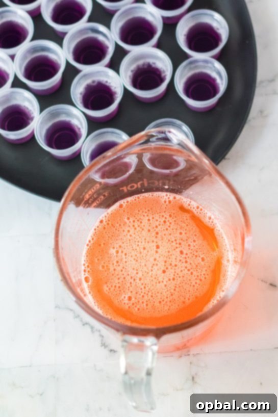 Halloween Spirit Shots 5 Pouring the vibrant orange Jell-O layer for a striking two-toned Halloween Jello Shot.