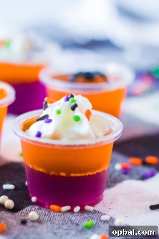 Halloween Spirit Shots 9 A tantalizing close-up of finished Halloween Jello Shots, garnished with whipped cream and festive sprinkles.
